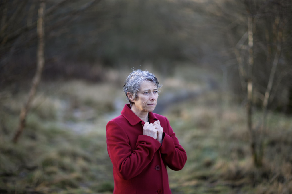 Maria Quinn standing in a forest wearing a red coat